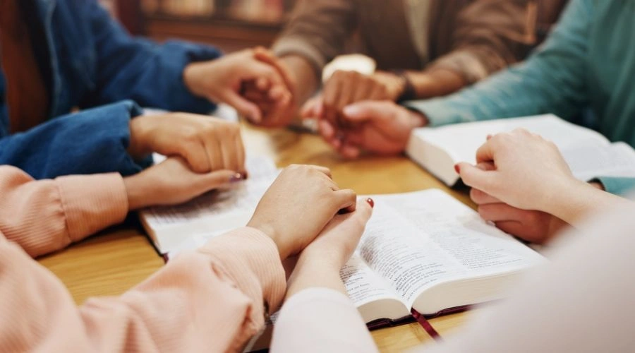 Group sitting holding hands and reading from the Bible