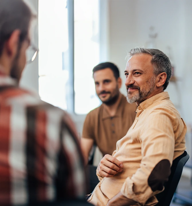 Transformative-Drug-and-Alcohol-Rehab-At-Changes-Healing-Center A group therapy session with three men seated in a circle, engaging in a supportive conversation in a bright room.