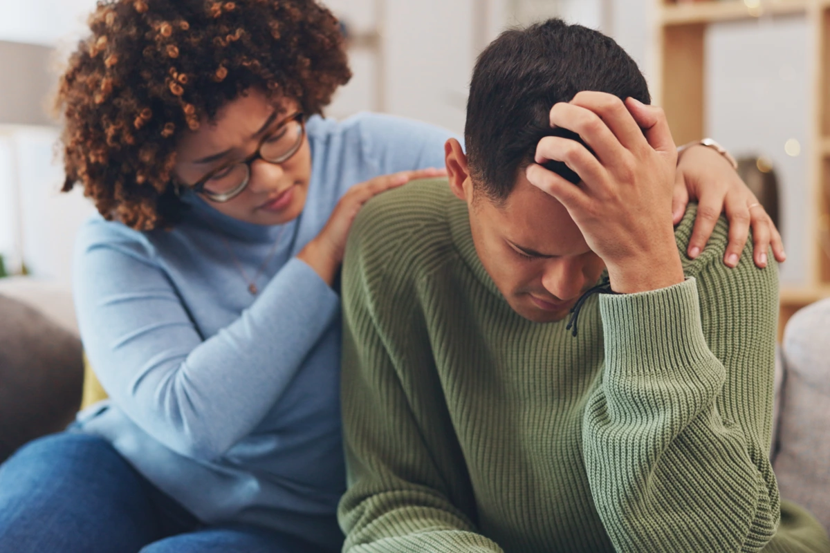 A caring woman rests a hand on a man’s shoulder as he struggles—gentle, trauma-informed support during addiction recovery at Changes Healing Center in Mesa, AZ.