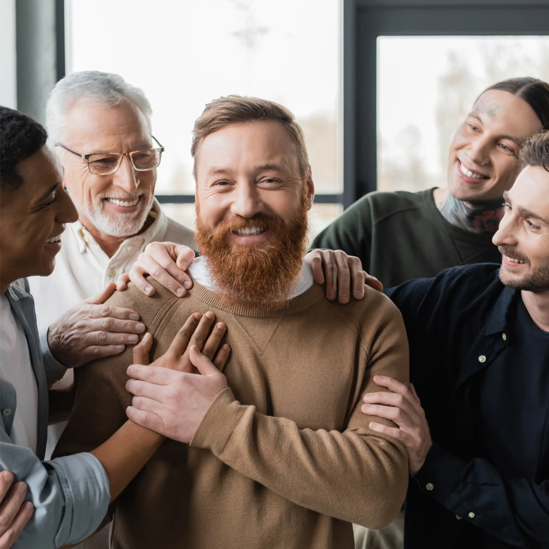 Smiling men in a bright room with supportive hands on shoulders—peer community in Changes Healing Center’s inpatient program in Arizona.