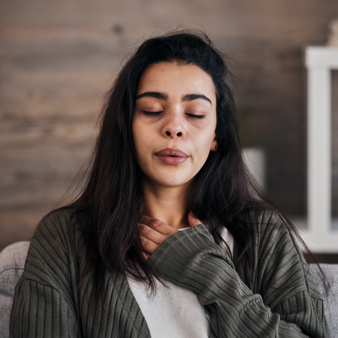 Woman sitting with eyes closed and hand on chest, appearing calm and introspective, representing emotional self-awareness and healing.