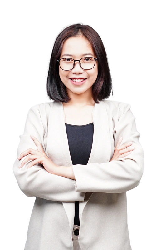 Smiling young woman with glasses and a beige blazer standing confidently with her arms crossed.